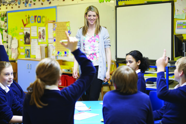 A teacher standing at the front of her room asking questions of her students acting as a professional tutor