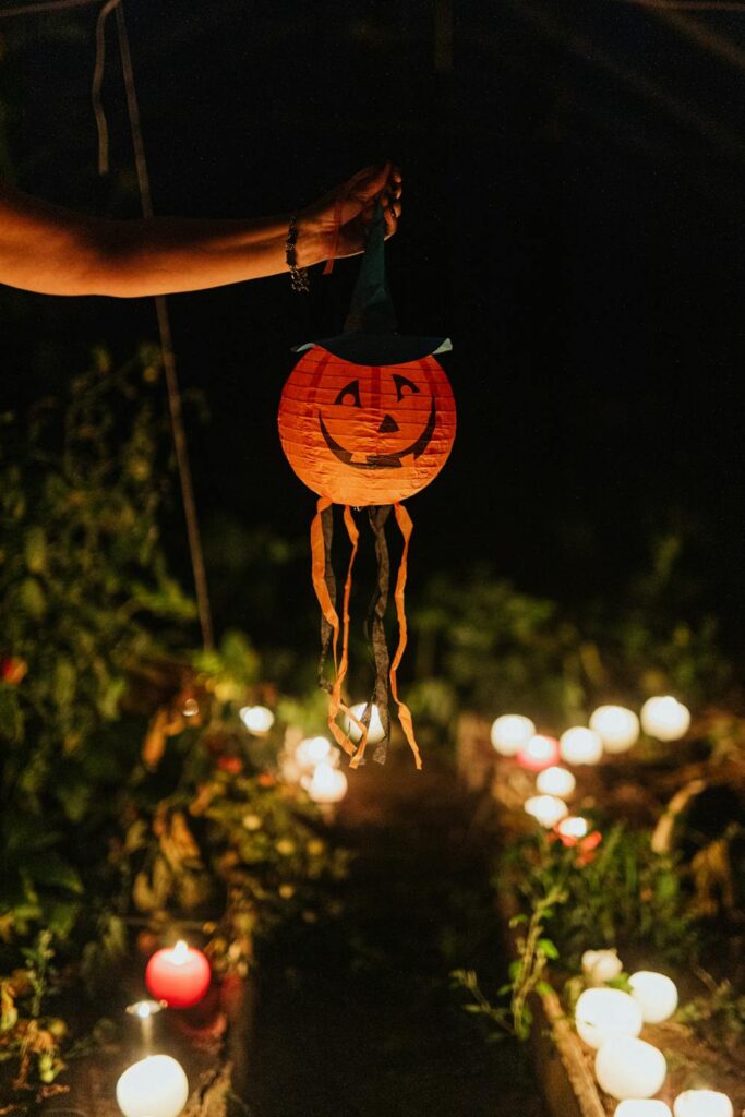 A person's arm and hand holding a jack o lantern Halloween lantern above some candles outside at night