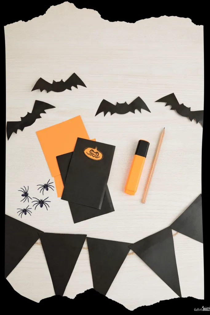 Supplies to make a DIY Halloween Party invitation including black and orange paper, a marker, tiny spiders and bats, and a pencil all on a white background