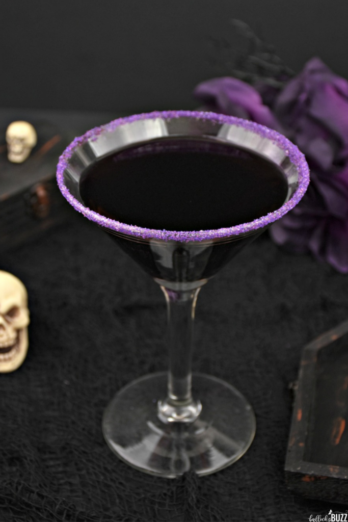 A purple Halloween cocktail in a glass with a purple sugar rim