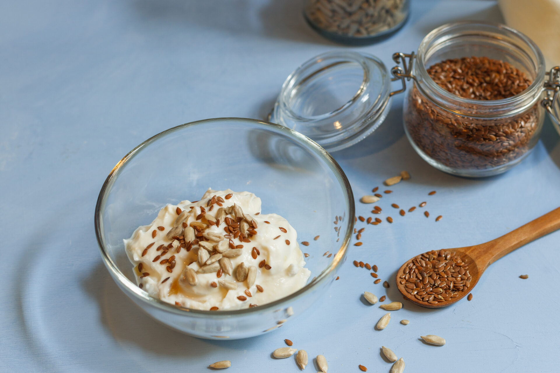 Soy yogurt with flax and sunflower seeds in a glass bowl and jars of seeds on a blue background close up with space