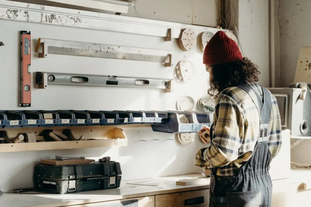 A person in overalls working on a project in front of a wall of tools.