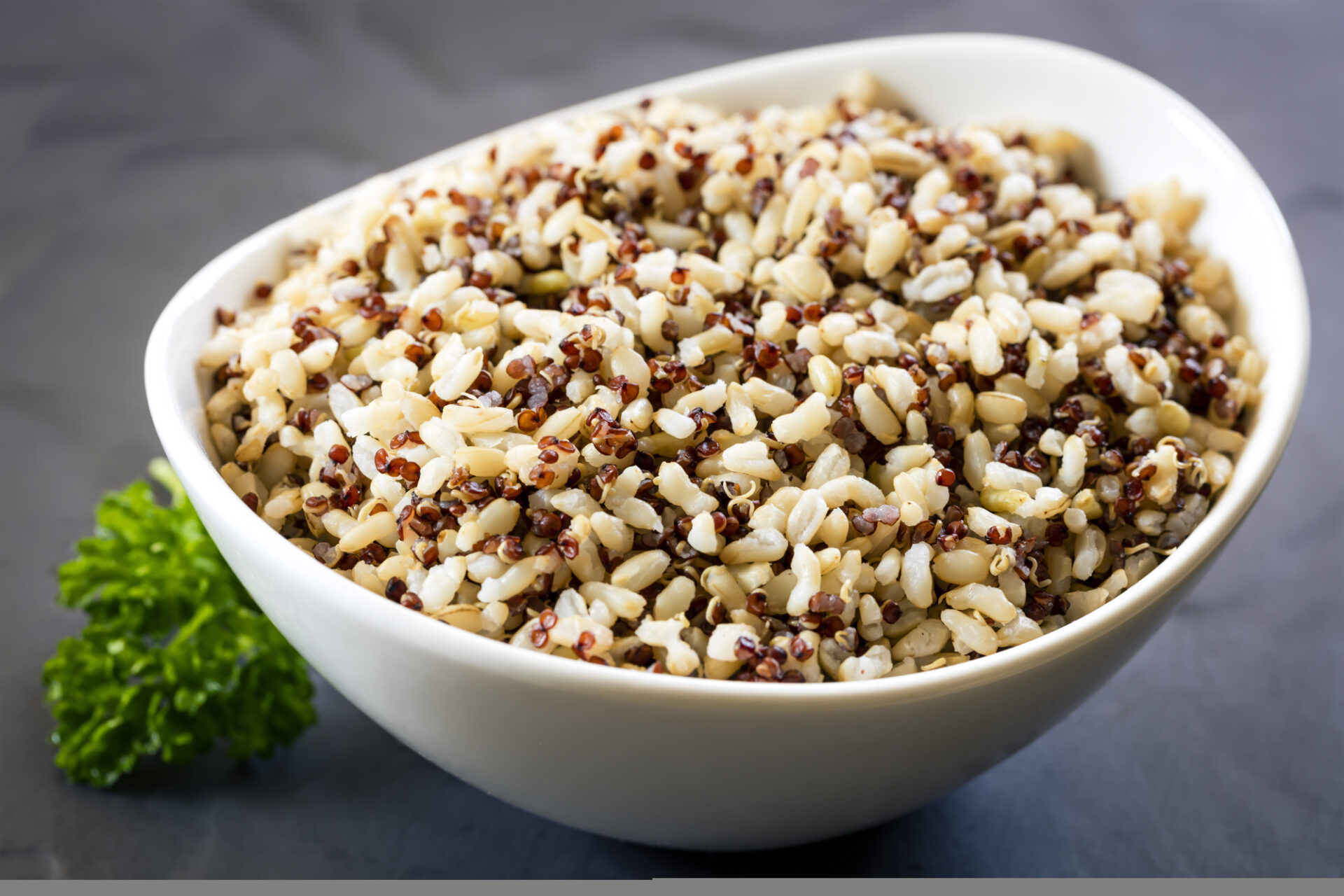 Brown rice and quinoa in white bowl over slate.