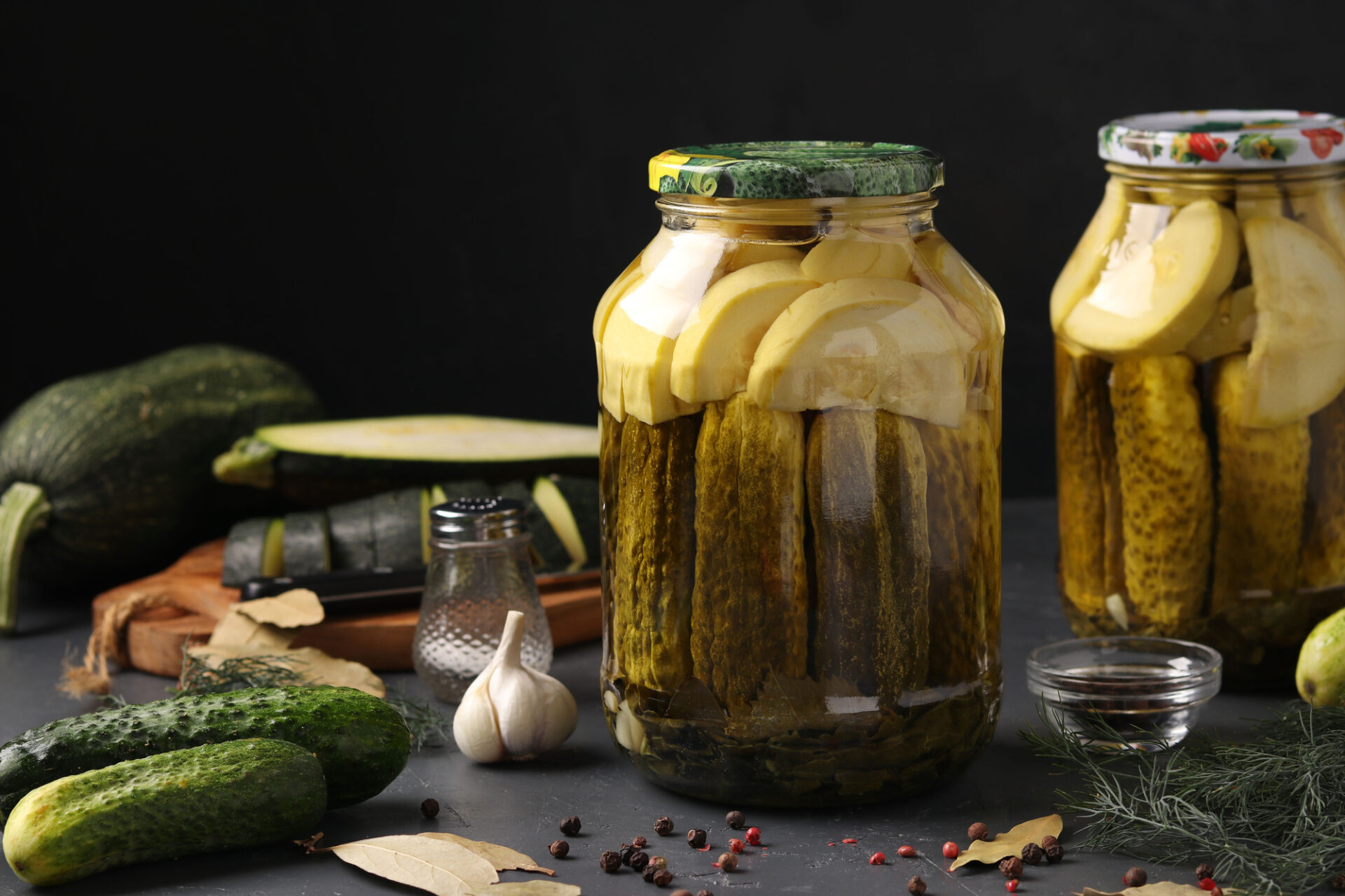 Marinated cucumbers and zucchini in jars on a dark background, horizontal format