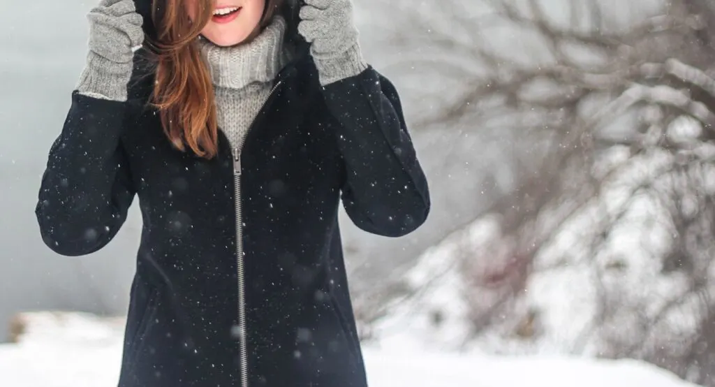 A woman in the snow wearing key winter wardrobe essentials including a coat, hat and gloves