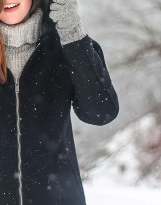 A woman in the snow wearing a thick coat, gloves and hat as part of her winter wardrobe essentials