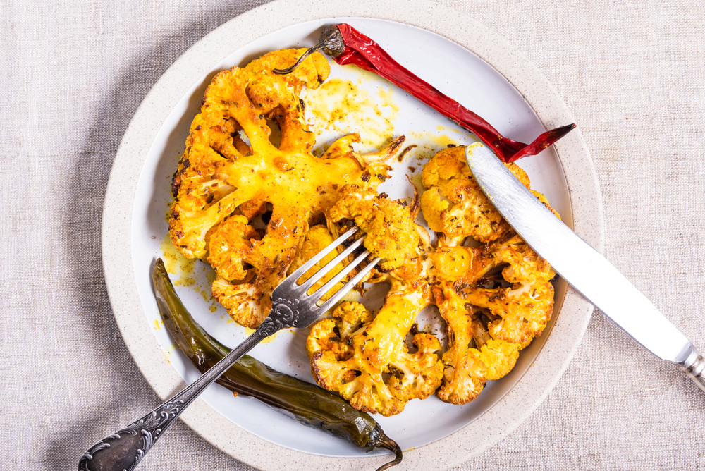 Tasty baked cauliflower steaks sprinkled with spices on a plate with chili pepper pods closeup - vegetarian cuisine