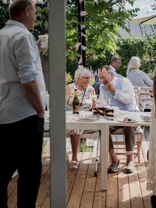 a group of people outside eating on the back deck of a home whilehosting the ultimate gathering