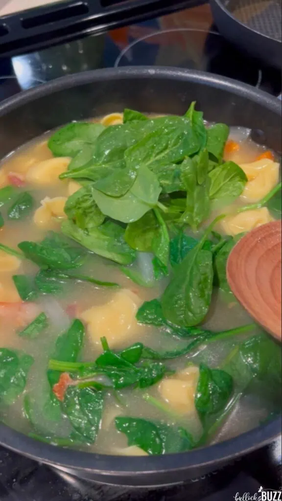 Adding fresh spinach leaves to the pot of Cheese Tortellini Soup with Bacon and Spinach