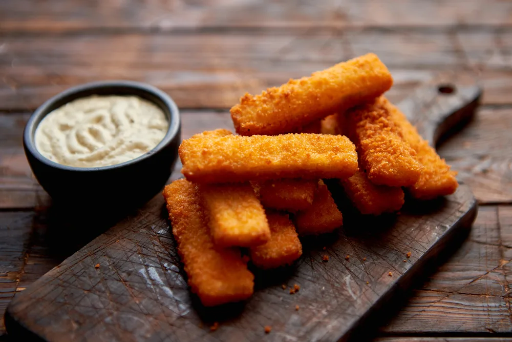 Pile of golden fried fish fingers with white garlic sauce — Photo