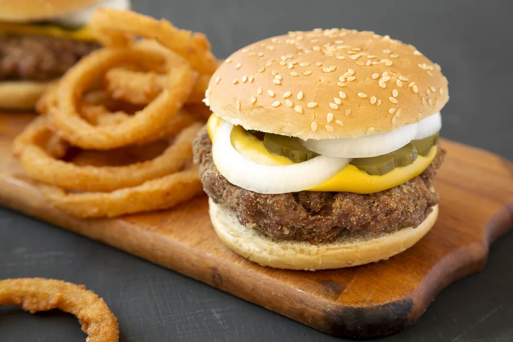 Homemade Mississippi Slug Burgers with onion rings on a rustic wooden board on a black background, side view. Close-up.