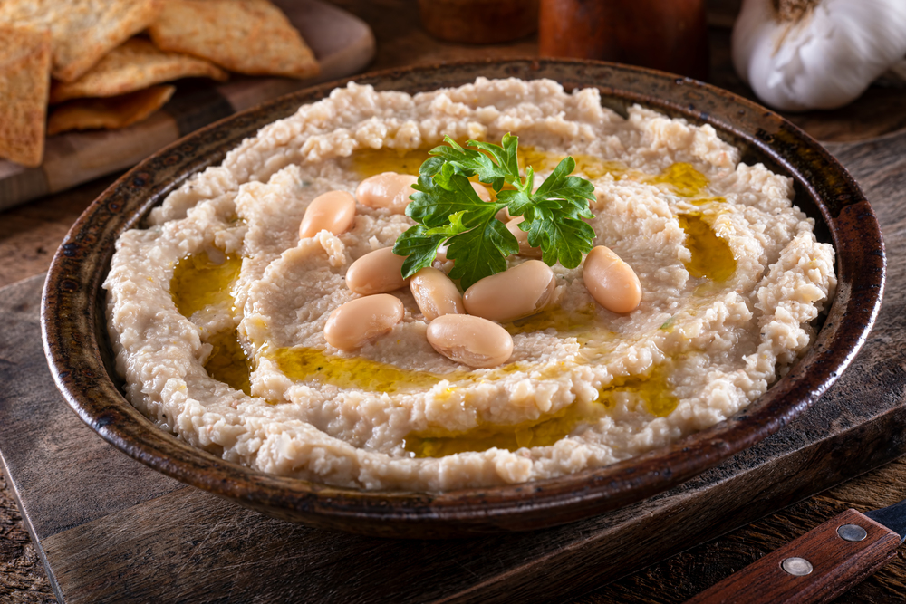 A bowl of delicious tuscan style white bean and garlic dip on a rustic table top.