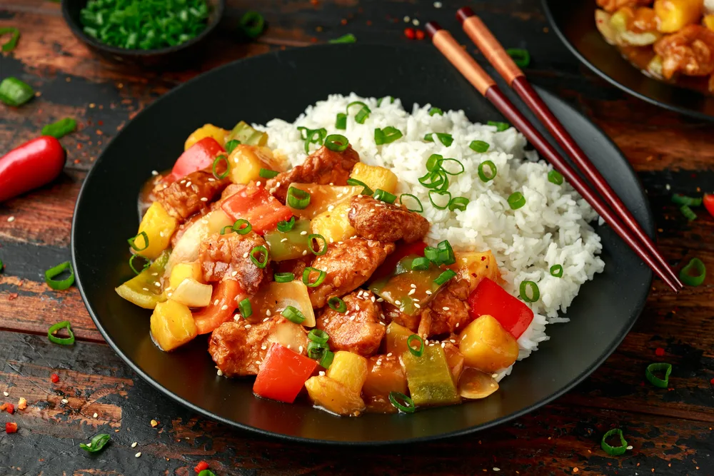 alt="Pineapple and Chicken in sweet and sour sauce with bell pepper, rice and spring onion on wooden table — Stock Photo, Image"