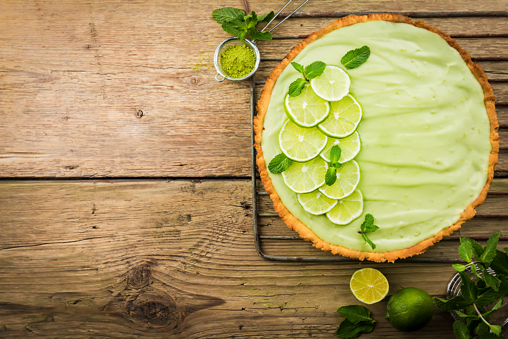 Key Lime Pie with several limes and mint over wooden background, top view with copy space.