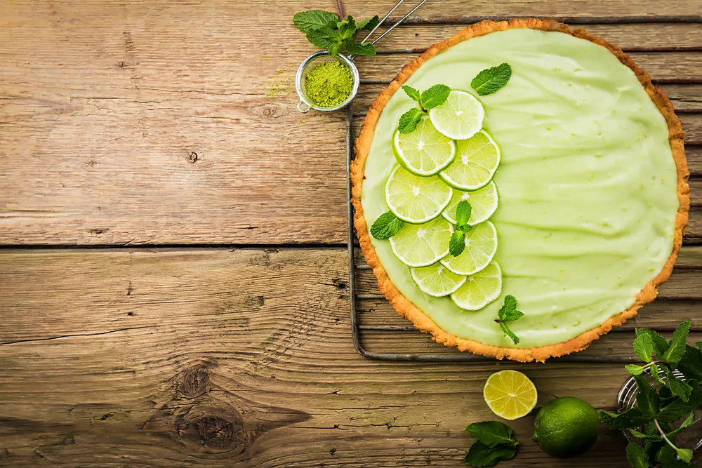 Key Lime Pie with several limes and mint over wooden background, top view with copy space.
