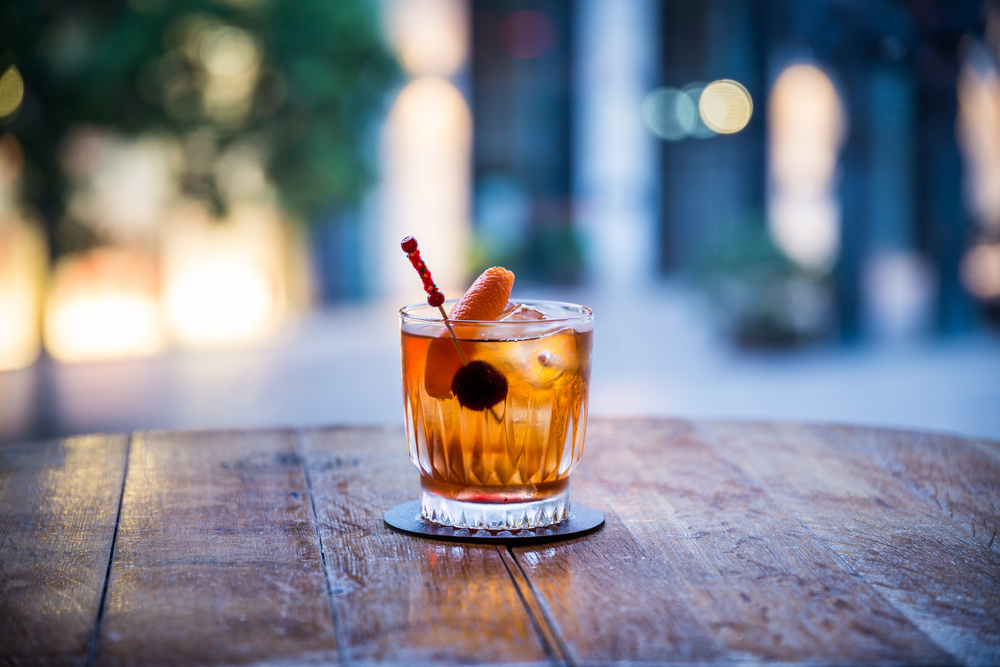 you can see a rum old fashioned on ice cocktail on a wooden table the color of which is orange transparent with a blurred background