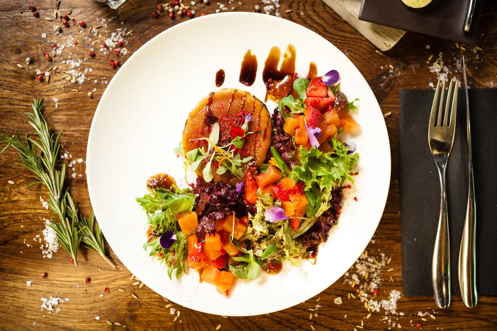 Goat cheese salad. Strawberry-melon salad with chilli, apple-orange sauce, fig jam on white plate. Delicious meat food closeup served on a table for lunch in modern cuisine gourmet restaurant.