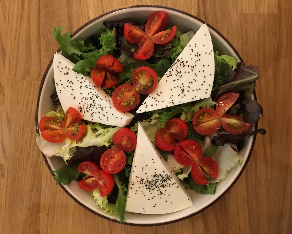 caprese salad bowl of lettuce, cherry tomatoes, caprese cheese and sesame grains view from top on a wood table