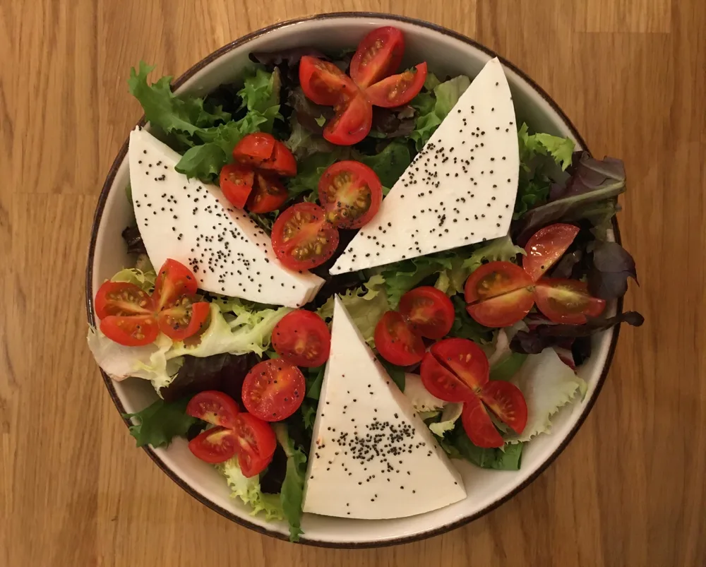 caprese salad bowl of lettuce, cherry tomatoes, caprese cheese and sesame grains view from top on a wood table