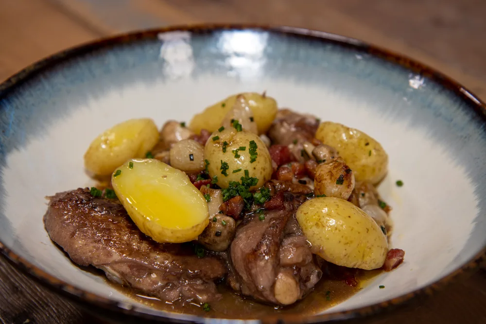 A delicious plate of chicken coq au vin with potatoes on a wooden kitchen work top