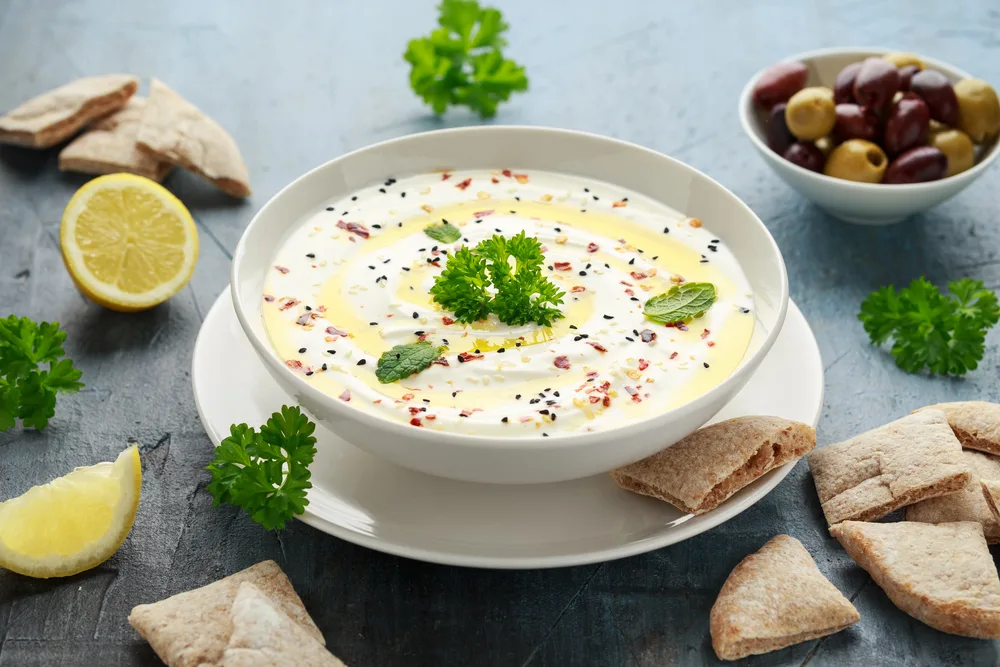 Labneh cream cheese dip with olive oil, salt, herbs served with olives, pita bread in white bowl — Stock Photo, Image