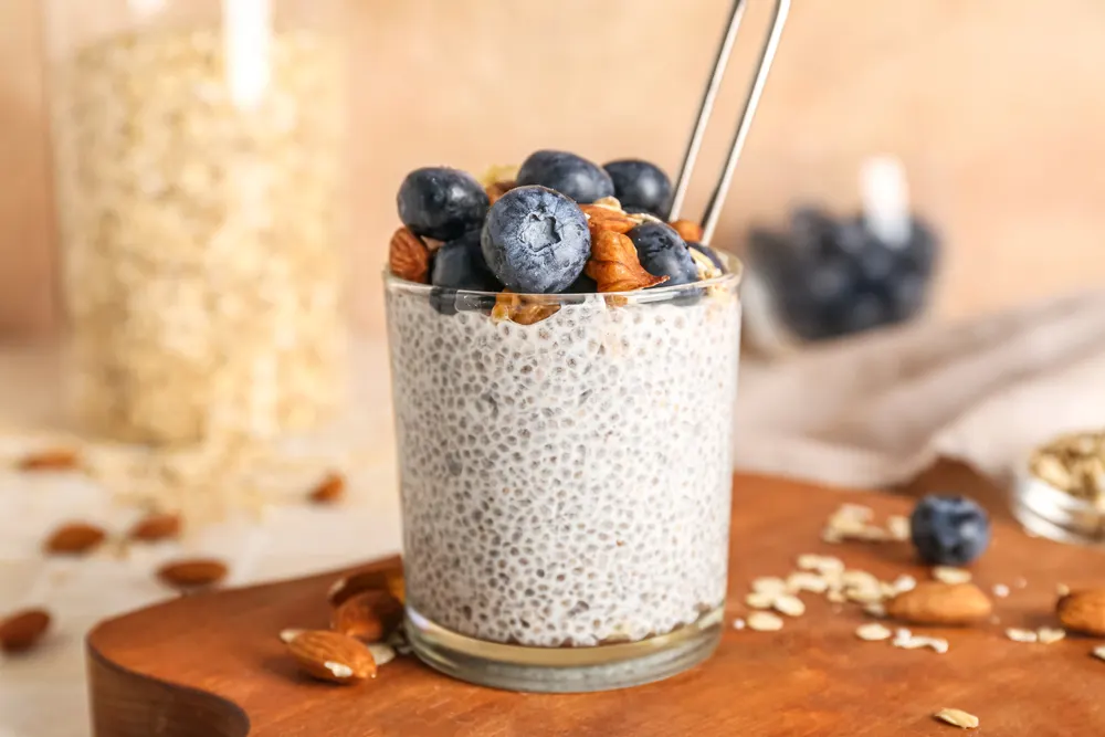 Wooden board with glass of tasty chia seed pudding and berries on table, closeup
