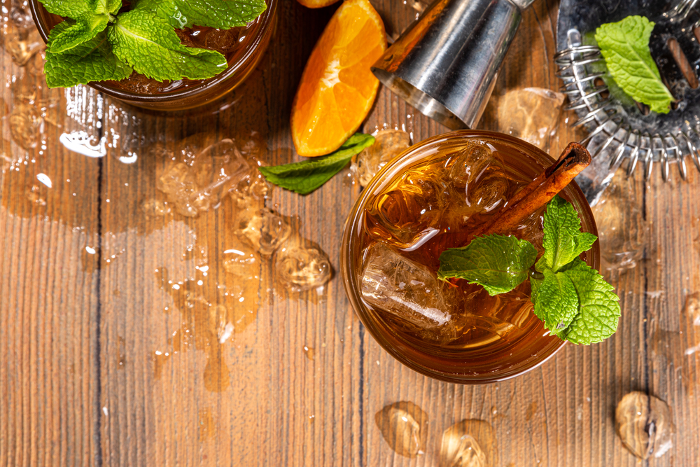 Autumn spicy booze alcohol drink, Tangerine Whiskey Smash cocktail with mint, cinnamon and tangerine slice on wooden background