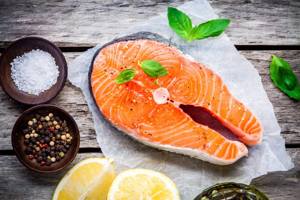 fresh raw salmon steak with salt, lemon, and basil on the rustic wooden table