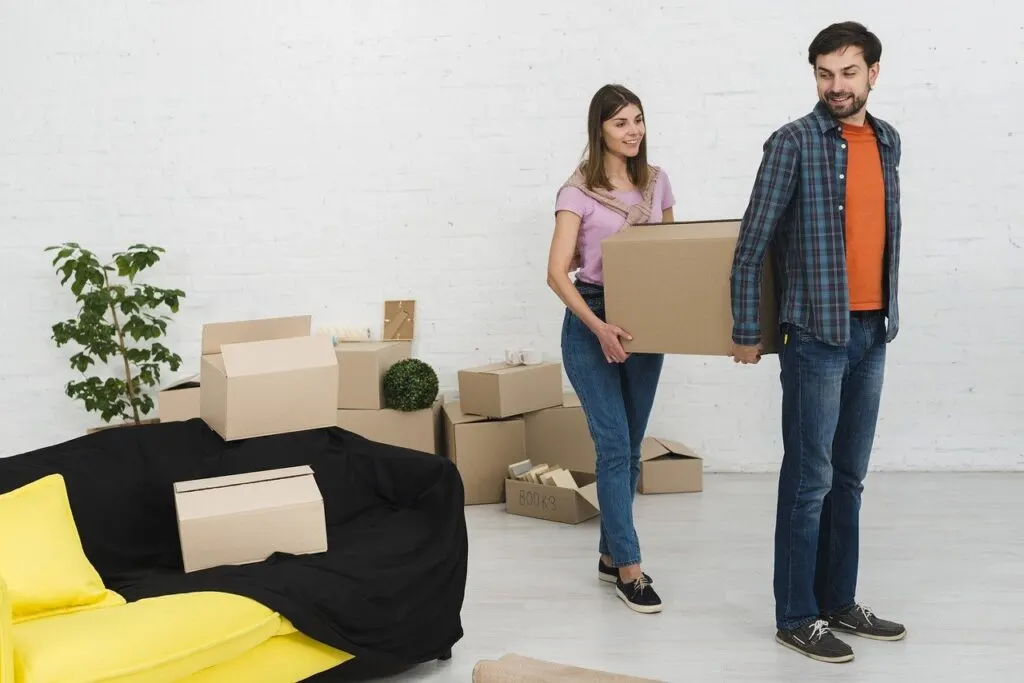 A couple carrying boxes out for their move can cause some common moving mistakes
