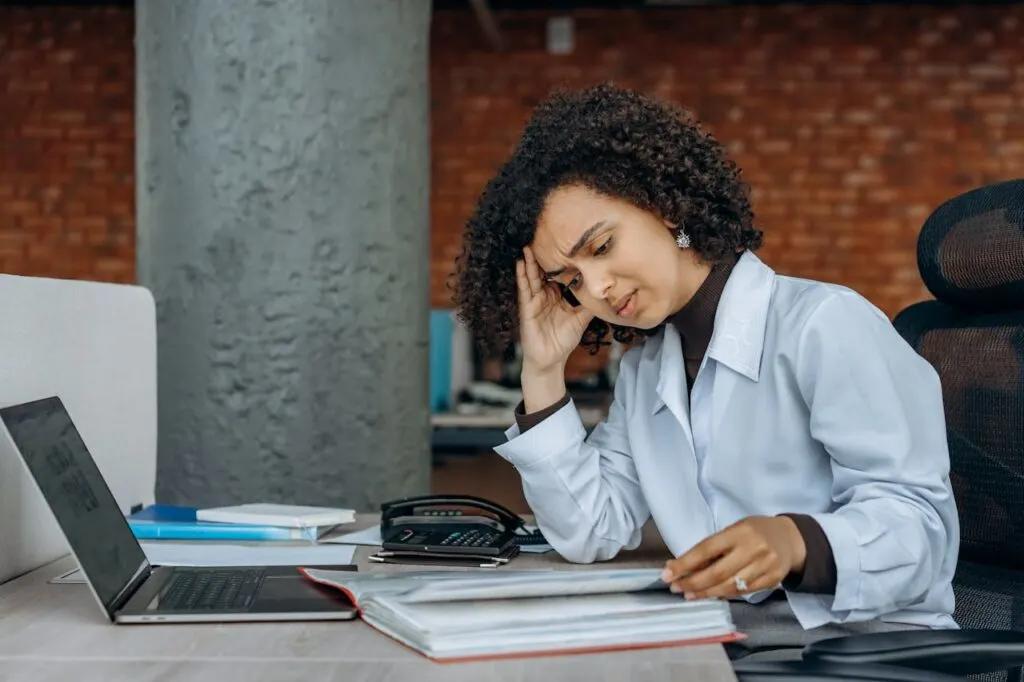 A woman sitting at her desk holding her head up and frowning due to post-Covid fatigue