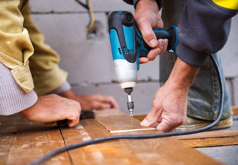 Handymen installing wooden flooring in patio, working with one of the must-have tools for DIYers, a drill