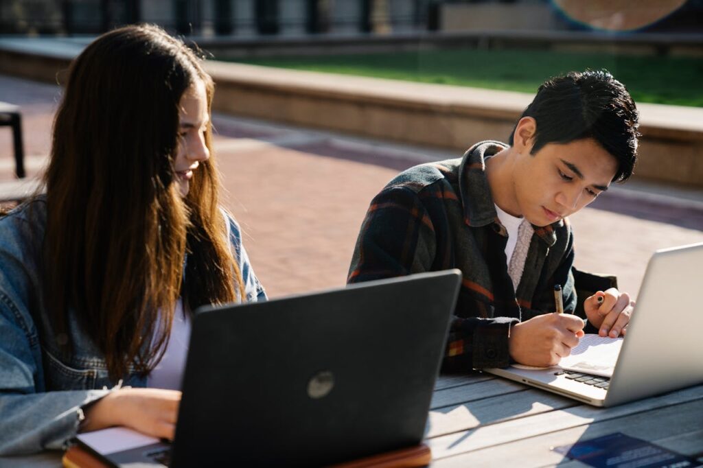 Two students working on laptops while sitting outside. Schools are making sure students have easy software access 