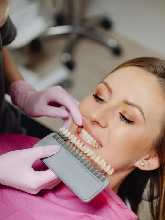 A dentist trying to match a crown to the same color in a woman's mouth in order to avoid a common cosmetic dentistry mistake
