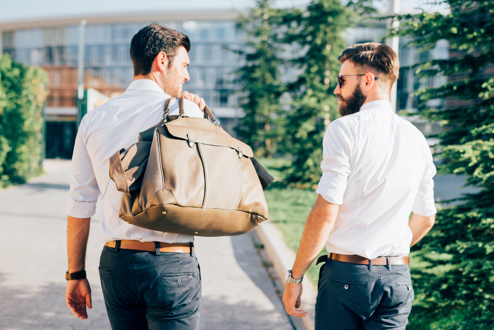 Rear view of two young blonde and black hair modern businessman, walking outdoor in the city part of the digital nomadism trend.