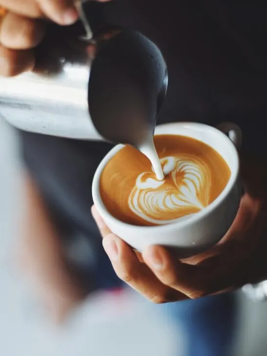 A person pouring cream in a heart shape into a cup of home brewed coffee.
