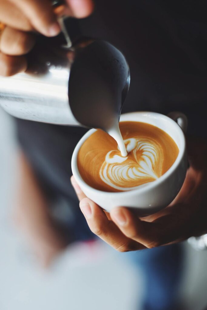 A person pouring cream in a heart shape into a cup of home brewed coffee.