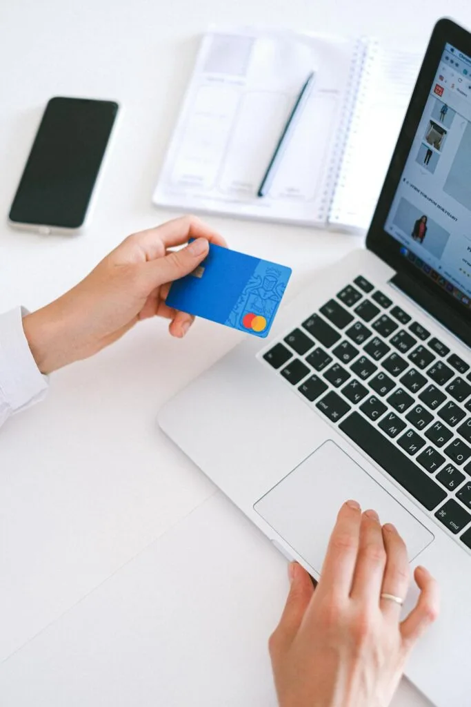 A person holding their debit card while typing on their laptop as part of the process to send money overseas
