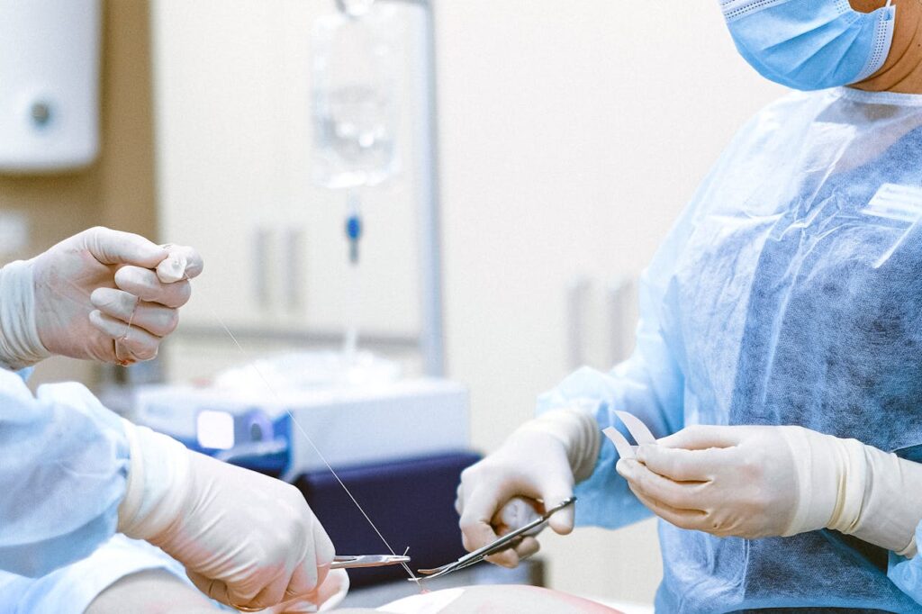 Two surgeons tying off sutures after performing plastic surgery as part of a person's aesthetic transformation.