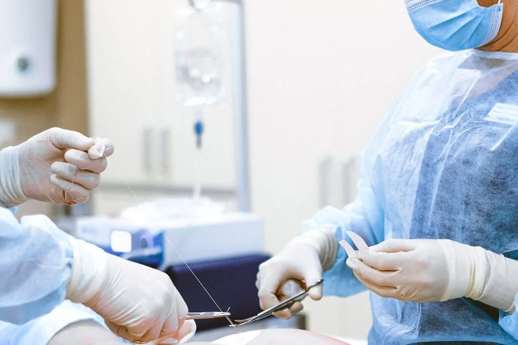 Two surgeons tying off sutures after performing plastic surgery as part of a person's aesthetic transformation.