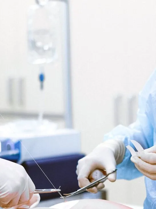 Two surgeons tying off sutures after performing plastic surgery as part of a person's aesthetic transformation.