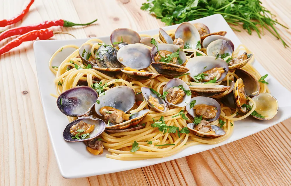 Pasta with steamed clams on white square plate