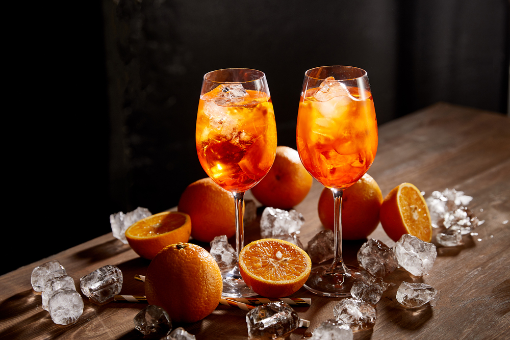 Aperol Spritz in glasses, oranges and ice cubes on black back