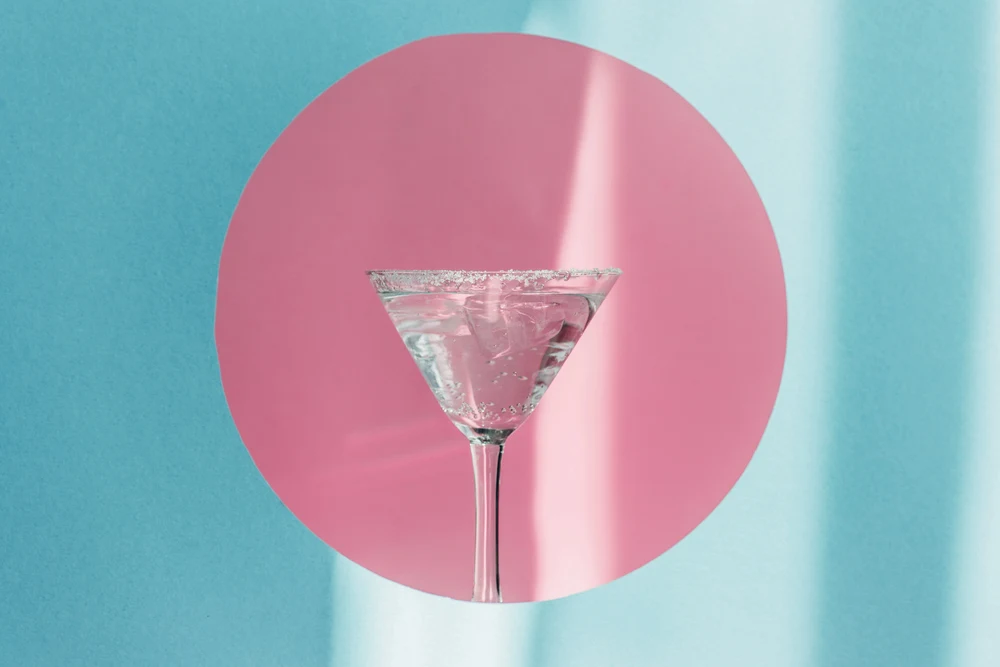 Gin and tonic in martini glass in pink circle on blue background