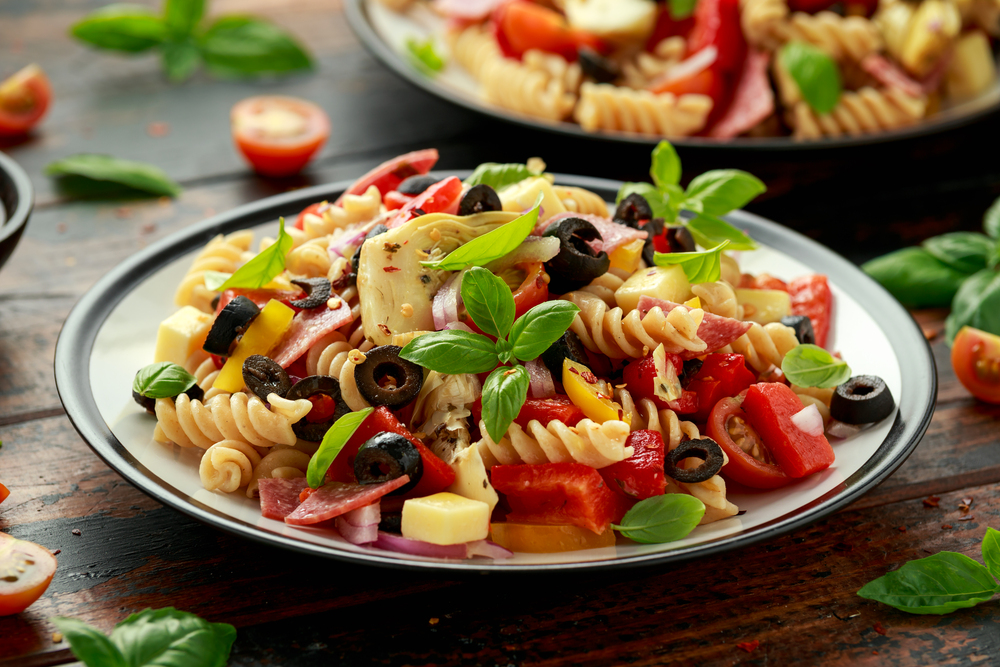 Antipasto salad with pasta, tomato, olives, red onion, bell pepper, salami, cheese, artichoke and basil. — Stock Photo, Image