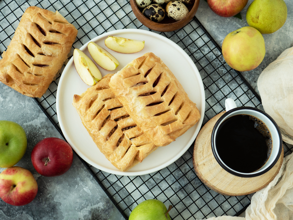 Top view food photography. Puff pastry pies with apples, brown sugar and eggs. Autumn baking with apple. Freshly baked apple rolls made from puff pastryand cup of coffee on a grey table. Soft focus — Stock Photo, Image
