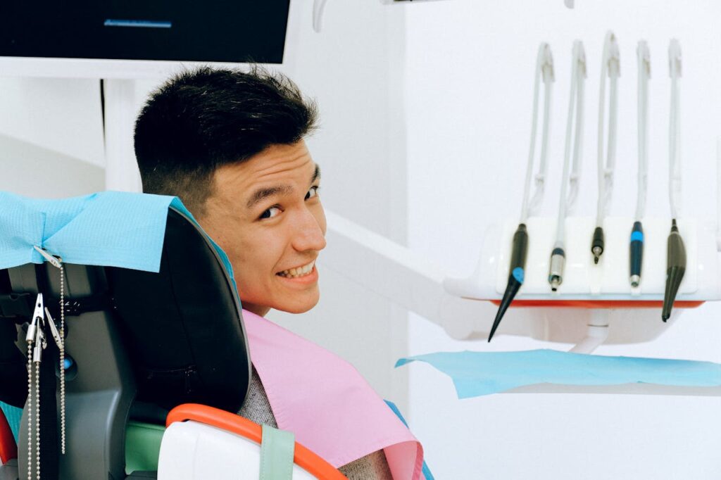 A guy sitting in a dentist's chair looking over his shoulder at the camera and smiling