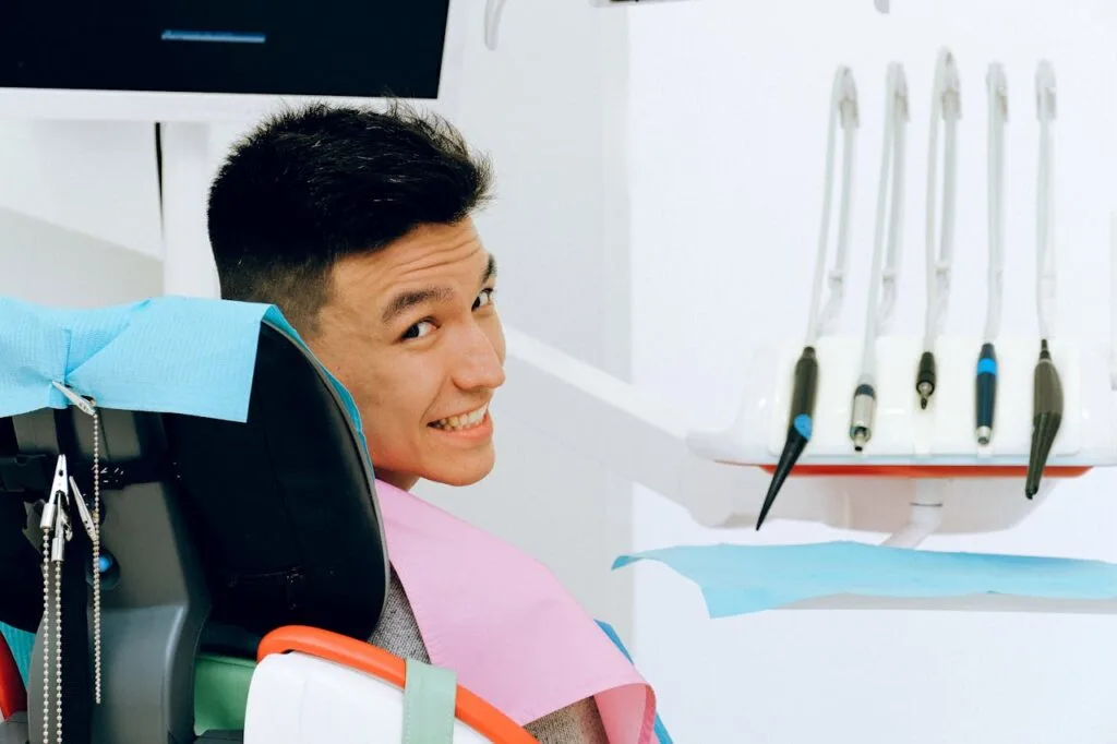 A guy sitting in a dentist's chair looking over his shoulder at the camera and smiling