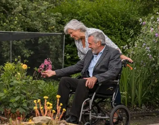 A man in a wheelchair in the garden with his wife. Here are some tips on caring for Older Parents with Limited Mobility