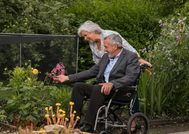 A man in a wheelchair in the garden with his wife. Here are some tips on caring for Older Parents with Limited Mobility