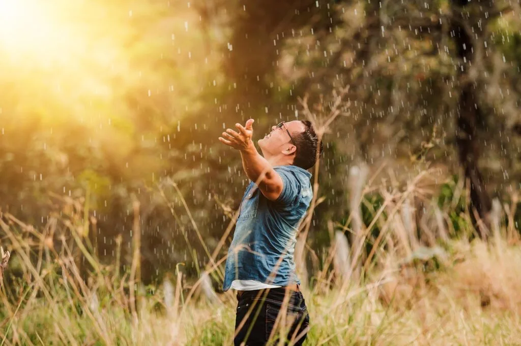 A man holding his arms out while standing in the rain in a field. Just one of the many ways to bring spontaneity into your daily routine
